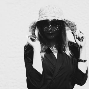 Portrait en noir et blanc d’une femme portant un chapeau, le visage partiellement voilé par des jeux d’ombre et de lumière.