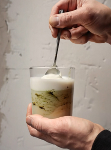 Mains tenant un verre contenant une boisson lactée verte, remuée avec une cuillère