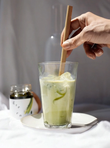 Main remuant une boisson verte avec des glaçons dans un verre posé sur une soucoupe