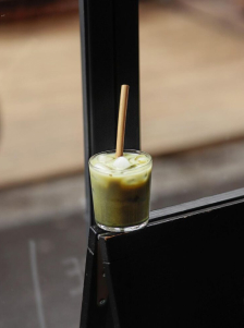 Verre contenant une boisson verte avec des glaçons et une paille, posé près d’une fenêtre